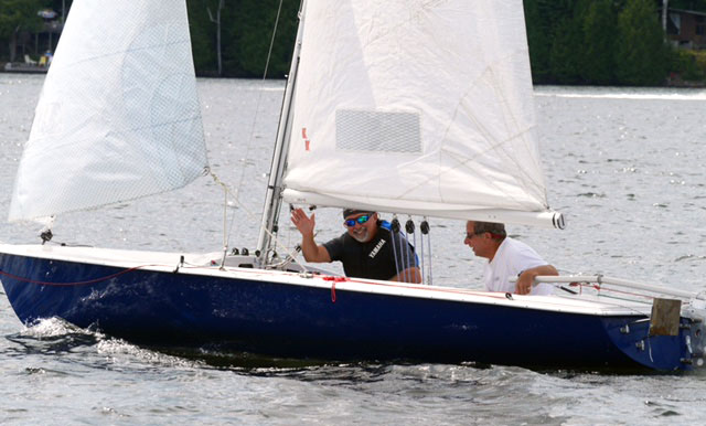 man waves from sailboat in a lake